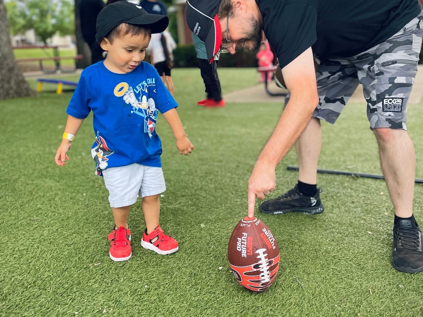 A volunteer helping a child with a football at an outdoor community event.